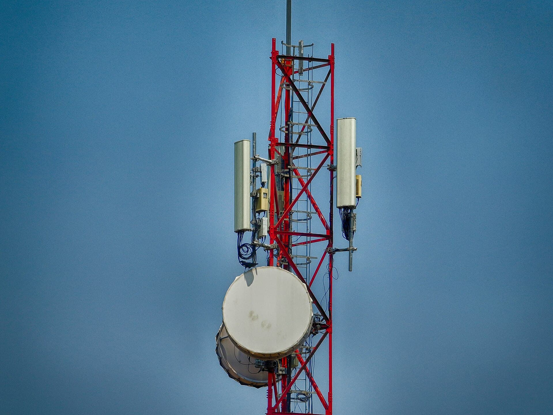 A lattice mast carrying panel antennas and a microwave dish against sky